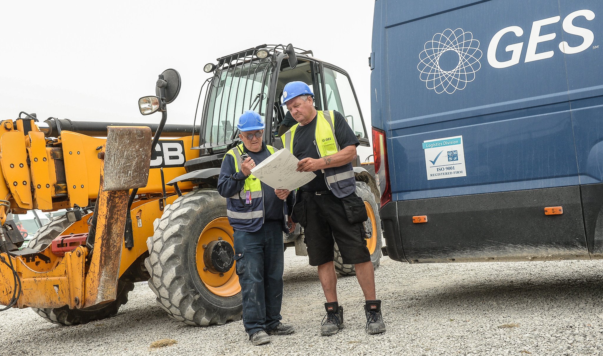 Deux membres du personnel de GES devant une pelleteuse et un véhicule logistique arborant le logo de l'entreprise.