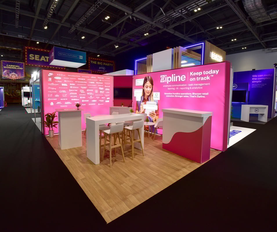Image of a pink coloured exhibition stand with booth backlighting on the show floor.