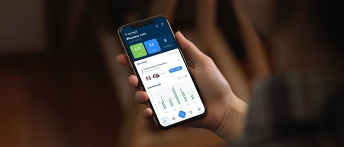 : Personne tenant un smartphone et utilisant l'application événementielle Visit par GES, qui affiche à l'écran des données sur l'événement et des informations sur les participant·e·s.